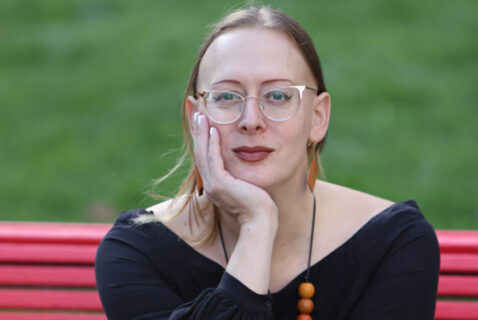 Headshot of Sasha Costanza-Chock, a nonbinary trans* femme sitting on a bench with their face resting on their hand.